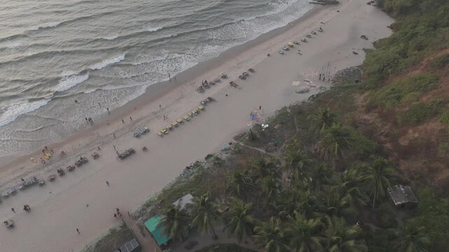 Aerial drone view of Arambol Beach showing coconut palms, white sand coastline, and gentle waves along the shore on a calm winter evening