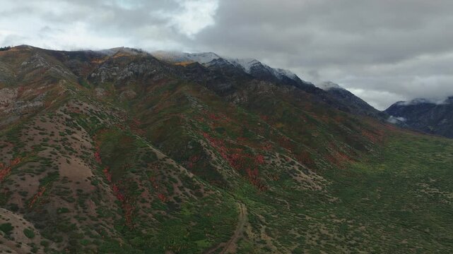 Aerial view of mountain range with vibrant fall colors contrasting with the snow-dusted peaks under a cloudy sky, Payson, Utah, United States.
