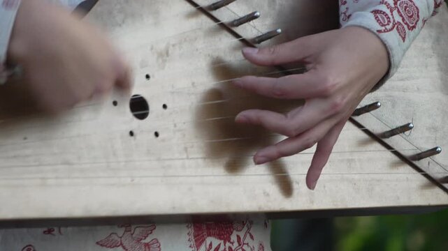 Gusli playing hands, woman performs traditional folk music outdoors, capturing cultural heritage