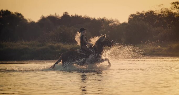 Super slow-motion footage of a rider galloping on horseback through shallow water at sunset. Dramatic splashes and warm golden light create a cinematic outdoor adventure scene.