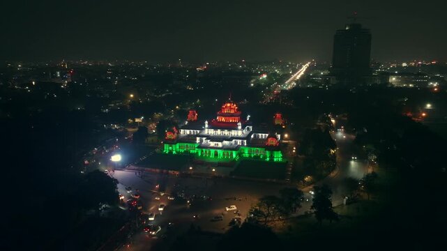 Aerial view of a grand building illuminated in vibrant colors at night, contrasting with the dark sky and the city lights, Ashok Nagar, Rajasthan, India.