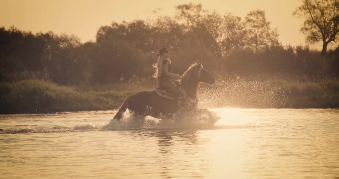 Super slow-motion footage of a rider galloping on horseback through shallow at sunset. Dramatic splashes and warm golden light create a cinematic outdoor adventure scene.