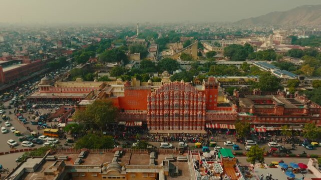 Aerial view of the intricate facade of the Hawa Mahal palace, with vibrant colors and bustling streets below, Jaipur, Rajasthan, India.