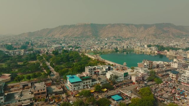 Aerial view of Man Sagar Lake and Jal Mahal against a backdrop of hills and buildings, showcasing a blend of natural beauty and urban landscape, Jaipur, Rajasthan, India.