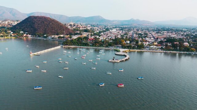 Aerial view of boats, a pier, and a dark mountain by the lakeside, contrasting with the city's buildings in the background, Chapala, Jalisco, Mexico.