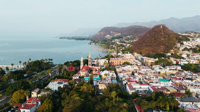 Aerial view of a town with a church and mountains, the serene lake reflects the sky, contrasting with the vibrant rooftops, Chapala, Jalisco, Mexico.