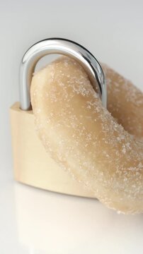 Bright reflective surface with sugared donut locked by metallic padlock placed centrally as symbolic food security context