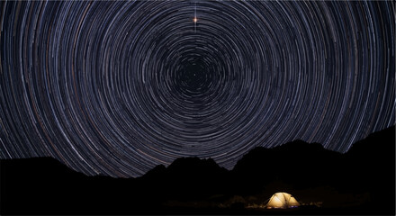 Fototapeta premium Lone campsite under a swirling sky of star trails and mountains