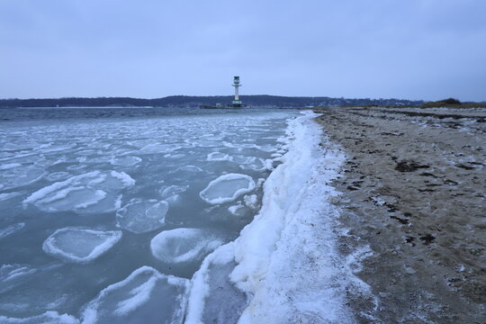 Falckensteiner Strand mit Leuchturm und Eisschollen im Winter.