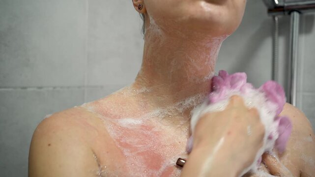 Close up of a woman washing her neck and chest with a soapy sponge in the shower