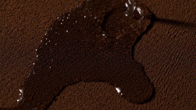 Close-up of clear water pouring onto a dark brown granular surface, spreading and being absorbed.