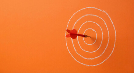 Red dart hitting the center of a target on orange background