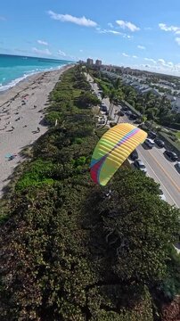 Aerial view of a paraglider soaring above lush greenery along the coast, contrasting with the blue ocean, Juno Beach, Florida, United States.