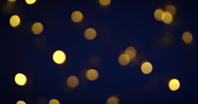 Blurred golden bokeh lights twinkle and create a warm, dreamy atmosphere on a dark blue background, perfect for festive and abstract purposes.