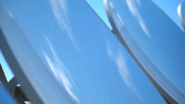 Close-up view of telecommunication satellite dishes with the sky's reflection on their metallic surfaces.