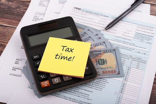 High angle view of calculator, dollar bill and 1040 tax form with adhesive note with text -Tax time