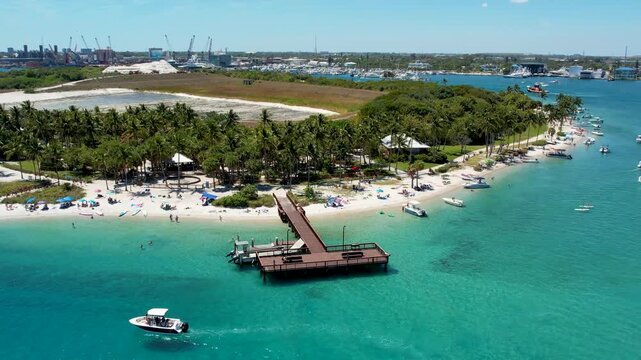 Aerial view of boats dotting the turquoise waters around Peanut Island, with a sandy beach contrasting with lush green trees, West Palm Beach, Florida, United States.