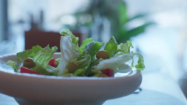 Fresh Green Salad Bowl On Table, Soft Daylight, Crisp Romaine Leaves, Olives And Cherry Tomatoes, Ceramic Bowl On Tabletop, Indoor Plant Bokeh, Slow Cinematic CloseUp, CleanEating Mood.
