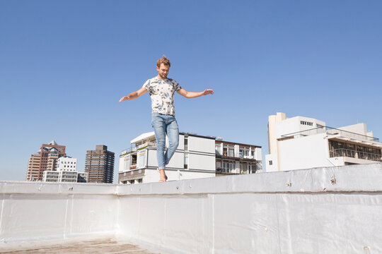 Barefooted man balancing on balustrade of a rooftop terrace