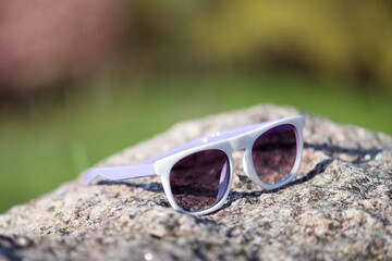 White sunglasses with purple lenses on rock in sunny outdoor setting
