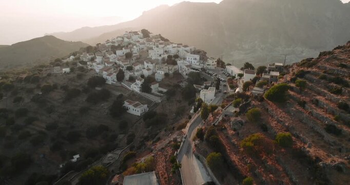 Aerial view of quaint white buildings clustered tightly on a hillside, bathed in the warm glow of the sun, Nikia, Kos, Greece.