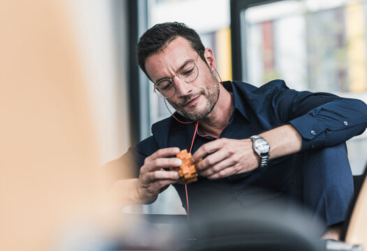 Mature man sitting in office assembling wooden cube puzzle
