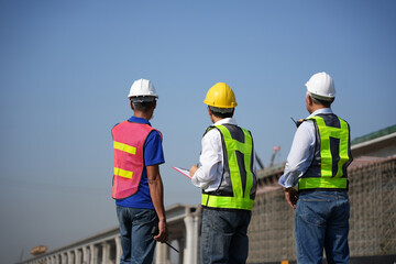 Construction supervisors reviewing project progress at infrastructure site, Engineering team inspecting bridge construction, Workers planning construction work at large infrastructure project