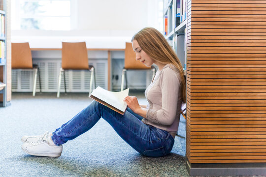 Teenage girl sitting on the floor in a public library reading book