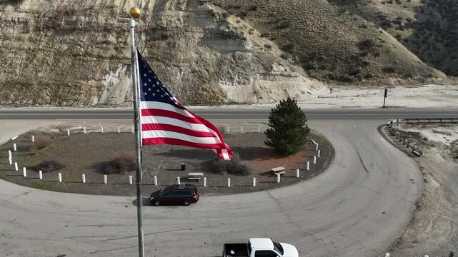 USA American Flag gentley waves over a parking lot in the desert next to a mountain highway. A mini van car has a solar panel on the roof