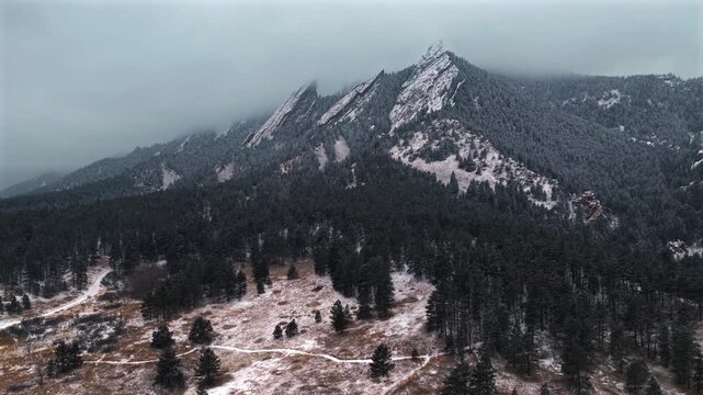 Flat Irons Mountain Winter Chautauqua Park aerial drone Colorado USA snowing snow flakes snowfall dusk sunset low clouds grass snow covered Rock formation walking loop trail Bear Peak backwards pan