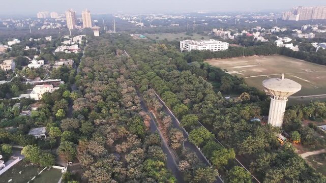 Aerial view of Greater Noida showing a water tower rising above dense green cover, with residential high-rises in the distance and light haze revealing the city&rsquo;s expanding urban landscape.