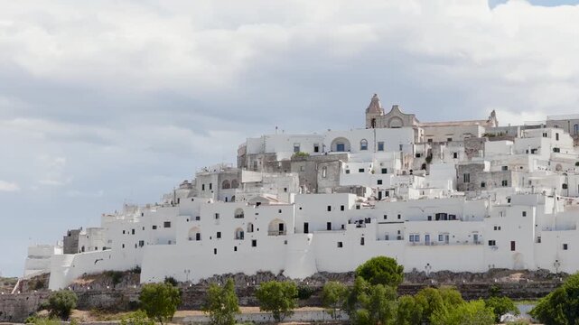 Aerial view of the beautiful, whitewashed buildings of Ostuni with a church prominent at the top, creating a stark contrast against the cloudy skies, Ostuni, Apulia, Italy.