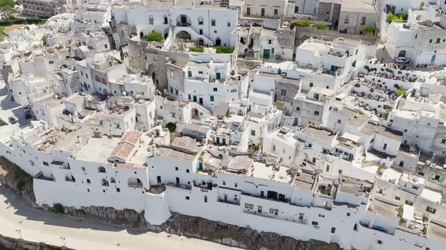 Aerial view of Ostuni's pristine white buildings cascading down the hillside, contrasting against the muted green landscape, Ostuni, Apulia, Italy.