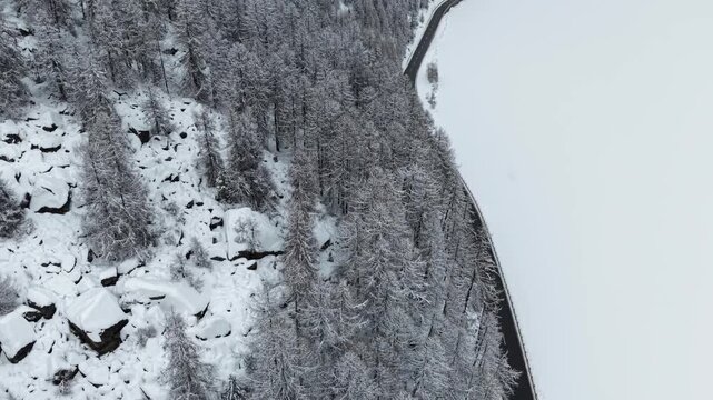 Aerial view of a road cutting through a snow-covered landscape, contrasting dark asphalt with white snow, near Sils im Engadin/Segl, Grigioni, Switzerland.