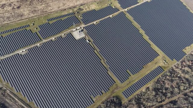 Aerial view of a vast solar panel farm with rows of dark panels contrasting against the surrounding dry fields, Wittelsheim, Grand Est, France.