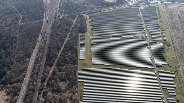 Aerial view of rows of solar panels reflecting the sunlight, contrasting against the adjacent bare trees, Wittelsheim, Grand Est, France.