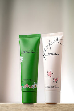 STRASBOURG, FRANCE - JANUARY 15, 2026 : A still life photographe of Marc Jacobs Daisy Wild and Perfect body lotion tube packaging. The product is displayed on a wooden surface, cream drapes background