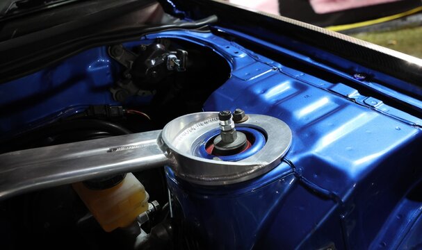 Close up of aluminum suspension strut brace bar on blue car engine bay shock tower