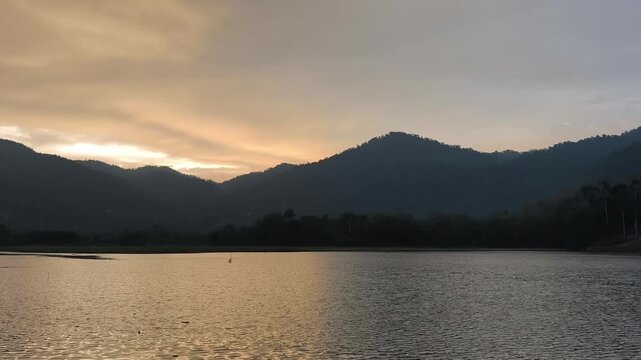 Static shot of lake and a bird seen flying over lake with hills and trees in tranquil natural setting.
