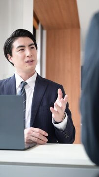 会社で商談や企画の営業をするスーツの男性、打ち合わせするビジネスマンの男性の縦動画	