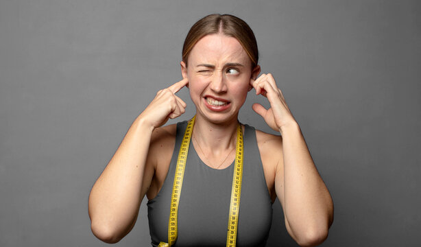 looking angry, stressed and annoyed, covering both ears to a deafening noise, sound or loud music. fitness concept
