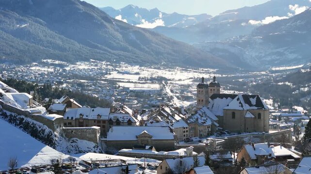 Aerial view of the snow covered Collegiate Church and buildings against a backdrop of majestic mountains, Briancon, Provence-Alpes-Cote d'Azur, France.