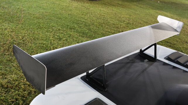 High angle close up of large matte black racing spoiler wing on white sports car