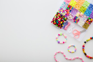 Bracelet, necklaces, scissors and case with colorful plastic parts on light gray table background. Closeup. Creating beaded jewellery for little child girl. Empty place for text. Top down view.