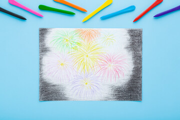 Drawn colorful fireworks on white paper. Wax crayon on light blue table background. Pastel color. Closeup. Little child handcraft. Top down view.