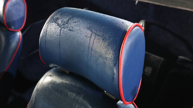 Close up of wet blue vintage car seat headrest with red piping covered in dew