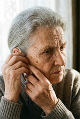 An elderly woman holds a hearing aid in her hand. The problem of hearing loss in old age.