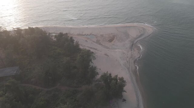 Aerial drone view of Querim Beach, North Goa, revealing a long sandy coastline with scattered rocky outcrops, rows of trees, and the Arabian Sea under soft winter evening light
