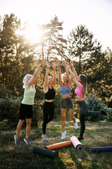Women exercising and jumping together outdoors, raising hands in celebration and joy. Group fitness, wellness, motivation and active lifestyle concept.