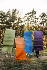 Women holding colorful yoga mats in front of their bodies outdoors in a park. Creative fitness concept, wellness, teamwork and healthy lifestyle.